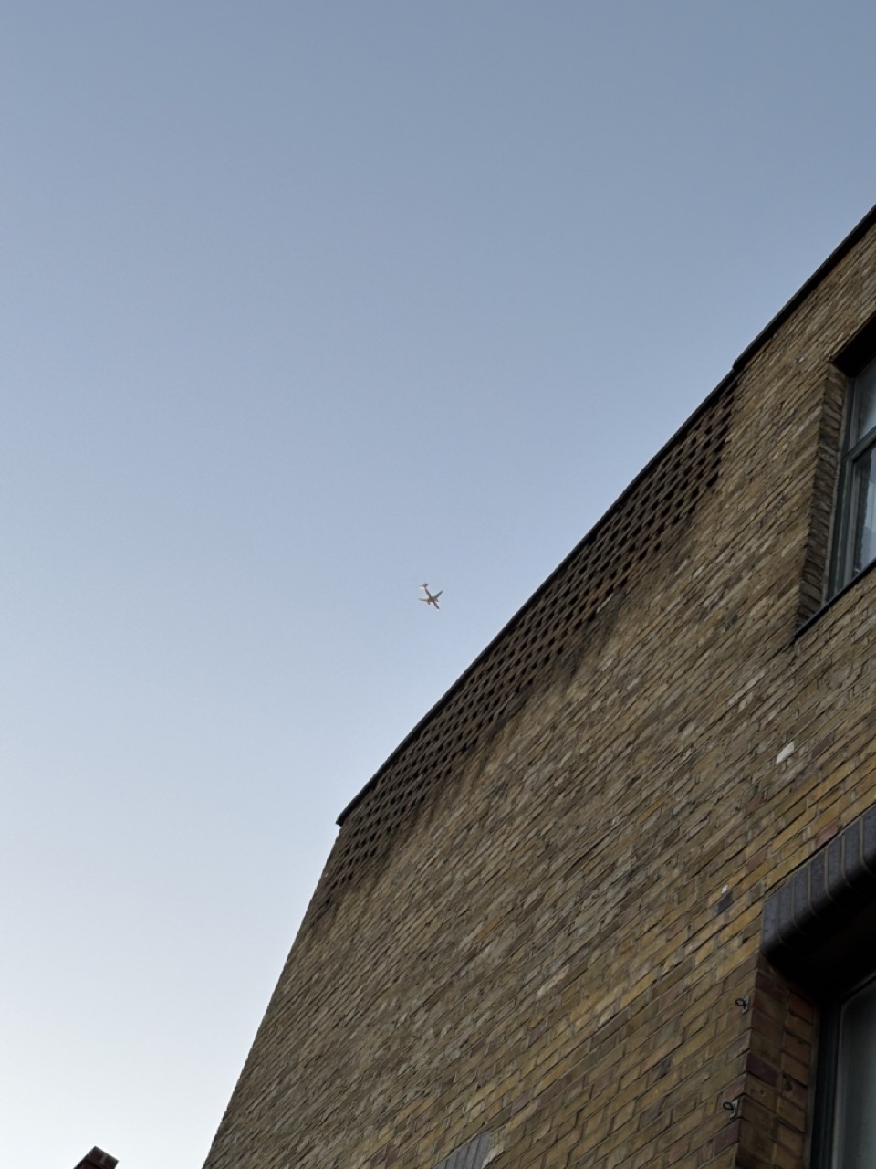 Photograph of building exterior and a plane passing overhead in a clear blue sky